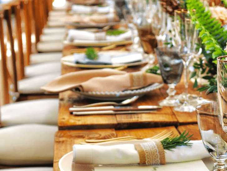 Lange gedekte tafel met glaswerk, servetten en groen voor een gezelschap